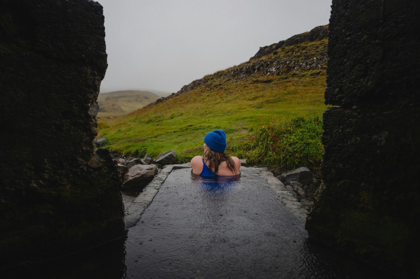 A woman resting in a geothermal pool in open hill country.